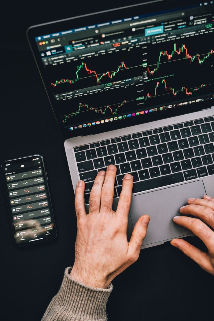home-img Hands typing on a laptop with cryptocurrency charts and smartphone display in view, focusing on digital finance.